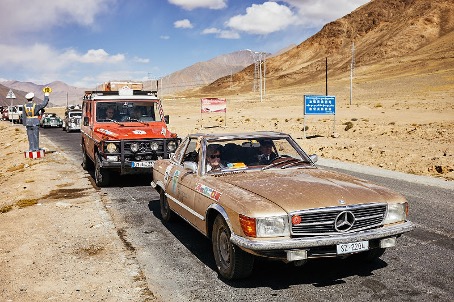 Mercedes-Oldtimer und Gel&auml;ndewagen mit Rallye-Aufklebern auf einer Stra&szlig;e im Hochgebirge, dahinter kahle Berge